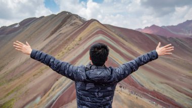 Asian Tourist raising hands up at Vinicunca Rainbow Mountain or Montana de Siete Colores, located on the road to the Ausangate mountain, in the Andes. famous travel destination in Cusco Region, Peru. clipart