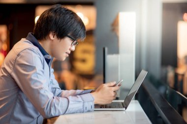 Asyalı işadamı akıllı telefon ve dizüstü bilgisayar kullanıyor. Erkek ofis çalışanı sosyal medya ve internet haberleri için mobil uygulama kullanıyor. İş stratejisi teknolojisi