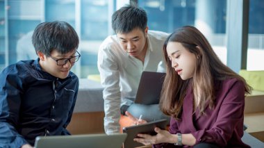 İş toplantısı ve takım çalışması konsepti. Asyalı iş kadını, iş yerinde sunum için dijital tablet kullanan meslektaşlarına proje veri raporunu açıklıyor. İş arkadaşları ofiste beyin fırtınası yapıyor.