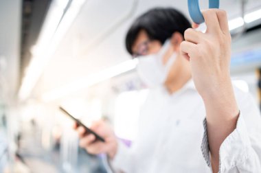 Asyalı bir adam hava treninde ya da şehir treninde akıllı telefon kullanarak cerrahi maske takıyor. Wuhan Coronavirus (COVID-19) toplu taşımacılıkta salgın önleme. Pandemik koruma için sağlık farkındalığı