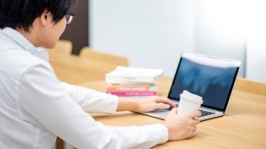 Evde online öğrenme kursu için dizüstü bilgisayar kullanırken elinde kahve fincanı tutan gözlüklü ve kulaklı Asyalı bir öğrenci. Karantina sırasında internette e-öğrenme. Herhangi bir konseptten çalış