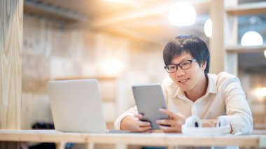 Zeki Asyalı iş adamı, karantina sırasında evde dizüstü bilgisayarla dijital tablet kullanarak çevrimiçi konferans yapıyor. Modern teknolojiyle akıllı çalışın. Telekomünikasyon ve internet kavramı