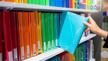 Kırtasiyedeki renkli raf görünümünden yeni açık mavi yüzük klasörü klasörü seçen erkek el. Ofis malzemeleri konsepti satın almak