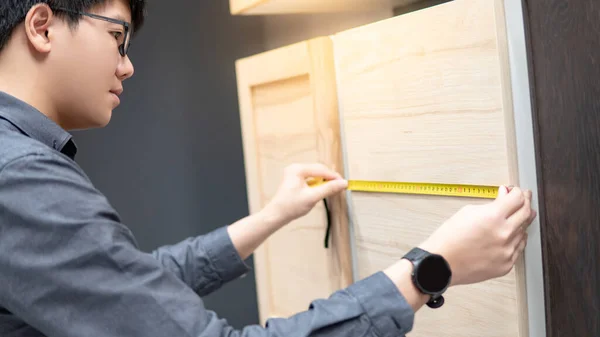 Asian man using tape measure on cabinet panel choosing materials or countertops for built-in furniture design. Shopping furniture and house decoration. Home improvement concept