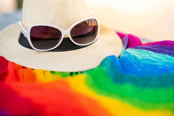 Sunglasses and Panama hat on rainbow scarf on tropical island beach. Accessories for summer travel. Summertime concept