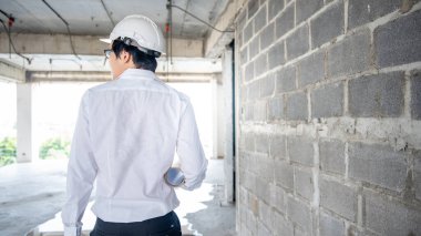 Asyalı inşaat mühendisi ya da koruma kaskı takan inşaat işçisi elinde yuvarlanmış planlar tutuyor. İnşaat alanında çalışan erkek mimar. İnşaat ve mimari tasarım kavramları