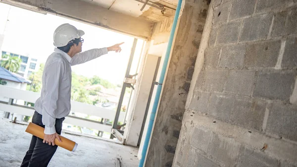 Asyalı inşaat mühendisi ya da koruma kaskı takan inşaat işçisi elinde yuvarlanmış planlar tutuyor. İnşaat alanında çalışan erkek mimar. İnşaat ve mimari tasarım kavramları