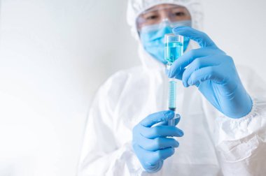 COVID-19 Aşı Konsepti. Coronavirus aşısı enjeksiyonu için şırınga ve ilaç şişesi tutan maske, gözlük ve lastik eldivenli kişisel koruyucu ekipman giysisi (PPE) giyen doktor veya hekim.