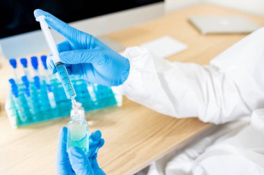 COVID-19 aşı araştırma konsepti. Coronavirus aşısı için hastane laboratuvarında şırınga ve ilaç şişesi tutan koruyucu lastik eldivenli doktor ya da tıp bilimci eli..