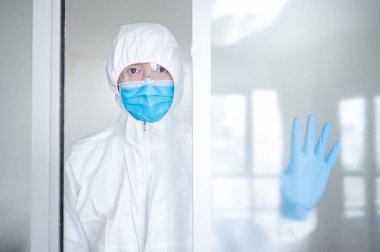 Hastane kliniğinin kapısında duran doktor ya da doktor kişisel koruyucu ekipman. Koronavirüsü (COVID-19) enfeksiyonunu önlemek için PPE giysisi, maskesi ve gözlüğü olan bir tıp çalışanı.