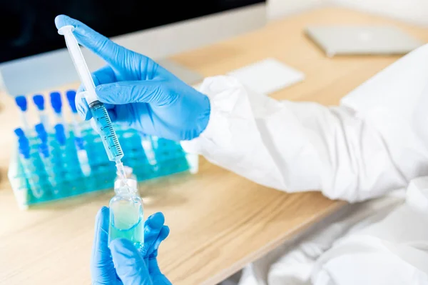 COVID-19 vaccination research concept. Doctor or medical scientist hand with protective rubber gloves holding syringe and medicine vial for Coronavirus vaccine injection test in hospital laboratory.