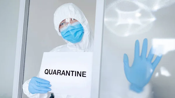 Doctor or medical worker in personal protective equipment (PPE) suit, mask and gloves showing paper with message Quarantine. Quarantine campaign during Coronavirus (COVID-19) pandemic