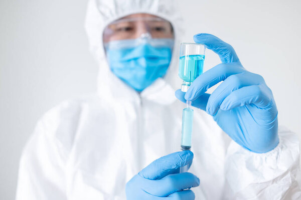 Концепция вакцинации COVID-19. Врач или врач в защитном костюме (СИЗ) с маской, очками и резиновыми перчатками, держащими шприц и медицинский флакон для инъекции коронавируса
.