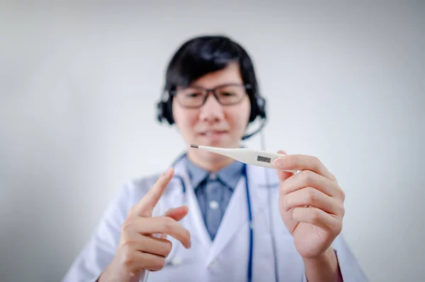 Measure body temperature concept. Male Asian doctor or physician man with glasses, stethoscope and headphones speaker teaching how to use digital thermometer with patient who is consulted from home.