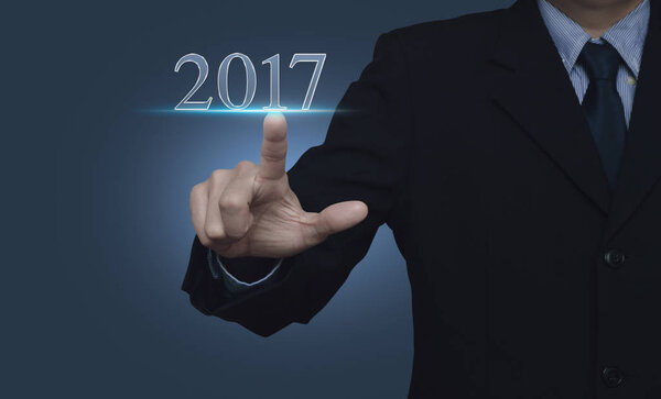 Businessman pressing 2017 text over blue background