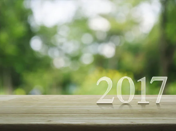 С Новым 2017 годом текст на деревянном столе над размытым зеленым деревом — стоковое фото