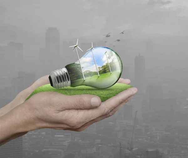 Light bulb with wind turbines and forest inside in hands — Stock Photo, Image