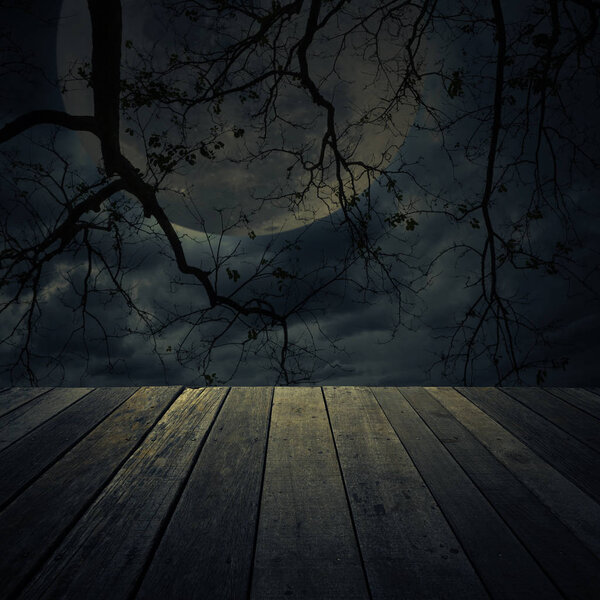 Old wooden table over dead tree, moon and spooky cloudy sky, Halloween background