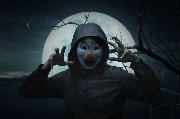 Gruseliger böser Clown trägt Jacke über Vogel, toten Baum, Mond und gruselig bewölkten Himmel, Halloween-Konzept — Stockbild Gruseliger böser Clown trägt Jacke über Vogel, totem Baum und Mond — Stockfoto