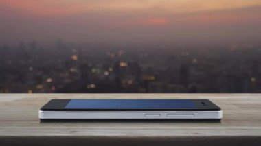 Harita pin düğmesi modern akıllı telefon ekranında ahşap masa üzerinde sıcak gün batımında şehir manzarası bulanıklığı, harita işaretleyici çevrimiçi konsepti