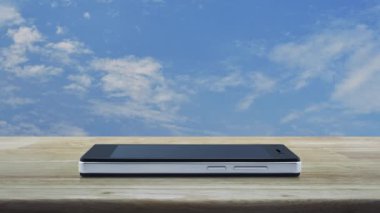 Beyaz bulutlar ile mavi gökyüzü üzerinde ahşap masa üzerinde modern akıllı cep telefonu ekranında Taksi araba düz simgesi, İş taşıma hizmeti online kavram