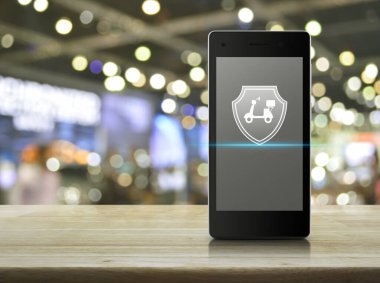 Motosiklet, kalkanın düz simgesi, modern akıllı cep telefonu ekranı, ahşap masa, bulanık ışık ve alışveriş merkezinin gölgesi, iş motosikleti sigortası, online konsept.