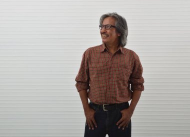 Gülümseyen Asyalı kıdemli iş adamı kırmızı gömlekli ve mavi kotlu beyaz duvar arkasında duran, iş başarısı konsepti