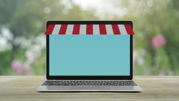 现代笔记本电脑与在线购物商店图形和木桌上的开放标志 园中模糊的粉红色花朵和树木 商务互联网商店的在线概念 — 图库视频影像