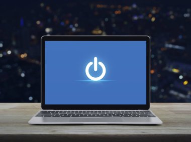 Elektrik düğmesi simgesi modern dizüstü bilgisayarda ahşap masada bulanık gece lambası ofis kulesi ve gökdelen üzerinde, online iş kurma kavramı