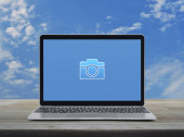 Kamera plochá ikona s moderním notebookem na dřevěném stole nad modrou oblohou s bílými mraky, Business camera service shop on-line koncept