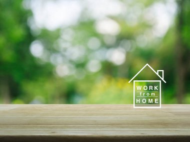 Bahçedeki bulanık yeşil ağacın üzerindeki ahşap masa üzerindeki ev simgesinden çalışmak, iş dünyasındaki sosyal uzaklık konsepti.