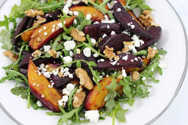 Arugula salad with beet, goat cheese and walnuts on white plate, horizontal image