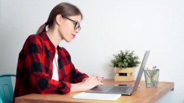 Genç beyaz bir kız öğrenci laptopunu kullanarak sıkı çalışıyor bazı sınavlara hazırlanıyor ya da evde ya da kütüphanede ödev yapıyor.