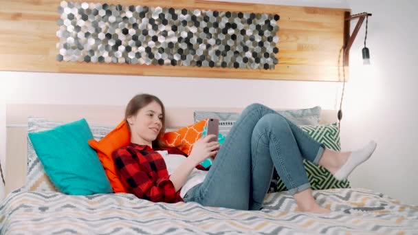 一位年轻貌美的白人女士正坐在现代卧房的床上 手里拿着平板电脑 一边发短信 一边用电子设备自拍了一会儿 — 图库视频影像