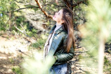 Genç ve şık bir kadın bir çam ağacının yanında duruyor ve gülümsüyor ve yukarıya bakıyor.. 