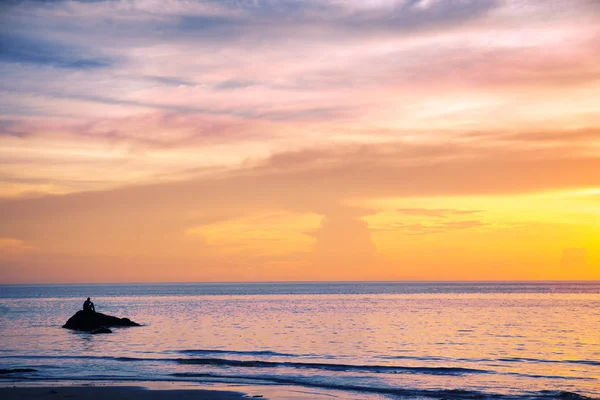 oturan ve gün batımında kayanın üzerinde düşünme adam