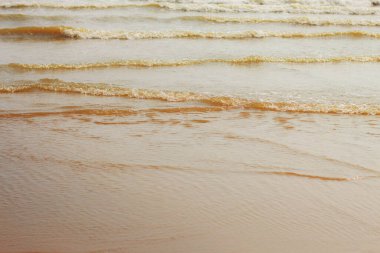 Kumsalda gün ışığında kum ve dalgalar.