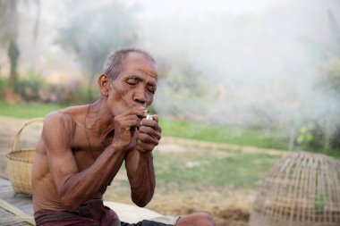 Tayland kırsalında sigara içen yaşlı bir adam..