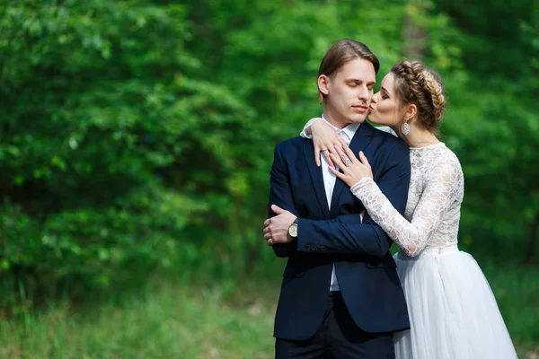 Νέοι όμορφη γαμπρός σε σκούρο μπλε κοστούμι και νύφη με λευκό crop top φόρεμα. Ευτυχισμένο ζευγάρι σε γάμο άνοιξη με τα πόδια — Φωτογραφία Αρχείου