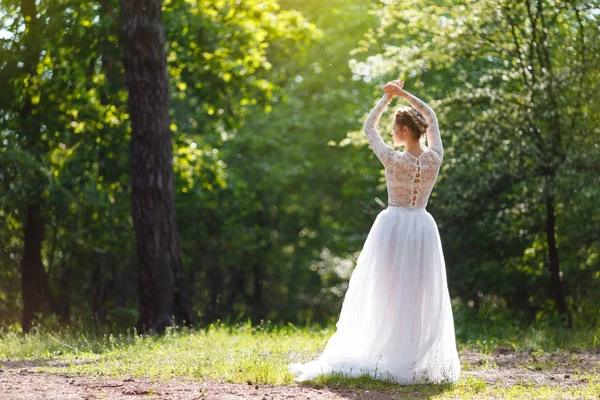 Молодая невеста стоит в парке спиной. Довольно необычная поза на камеру — стоковое фото