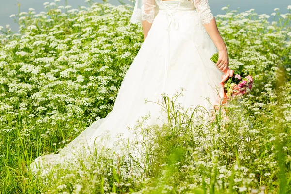 Невеста в белом платье в парке со свадебным букетом в руках — стоковое фото