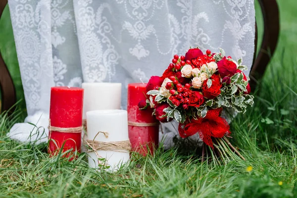 Dure, trendy bruiloft boeket rozen in marsala en rode kleuren die permanent op het gras in de buurt van grote kaarsen. Bruids details en decor met bloemen — Stockfoto