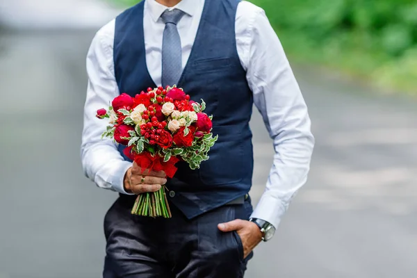 Brudgummen håller i händerna fina, dyra, trendiga Bröllopssvit Bröllop bukett blommor i marsala och röda colorsry kopplade till den blå kostymen — Stockfoto