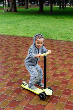Yağmurda sırılsıklam, bir çocuk bir sporda paten bir scooter üzerinde takım elbise. Bahar yürüyüşte şehir Park, yağmurlu hava