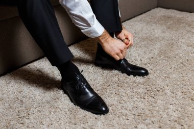 Koyu siyah pantolon ve beyaz gömlek ayakkabı ayakkabı bağı bağlayan bir işadamı. Modern, şık ve pahalı bak genç adam için.