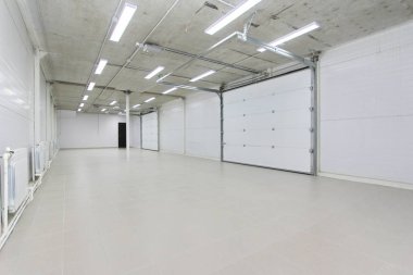empty parking garage, warehouse interior with large white gates and gray tile floor clipart