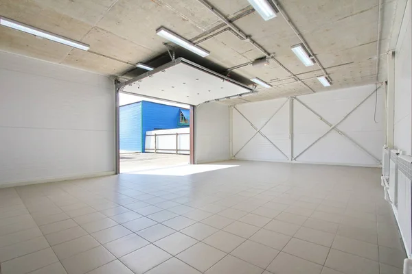 Пустой гараж, складской интерьер с большими белыми воротами и серым полом плитки — стоковое фото
