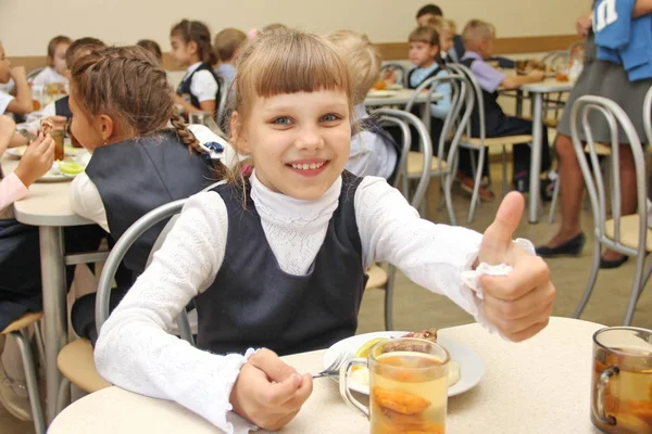 neşeli kız öğrenci oturma, tablo içinde okul kafeterya yemek yemek, içme suyu ve gösterileri başparmak yukarıya - Rusya, Moskova, ilk lise birinci sınıf b - 30 Eylül 2017