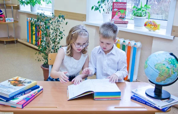 Två små skolbarn, pojke och flicka sitter tillsammans vid skrivbordet i klassrummet, läsa studien boken - 2 klass b - 28 oktober 2017, första gymnasiet, Moskva, Ryssland — Stockfoto