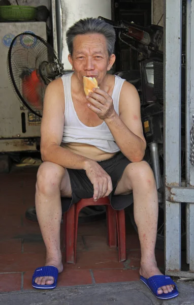 Vietnamita hombre está sentado en un taburete y comer pan —  Fotos de Stock